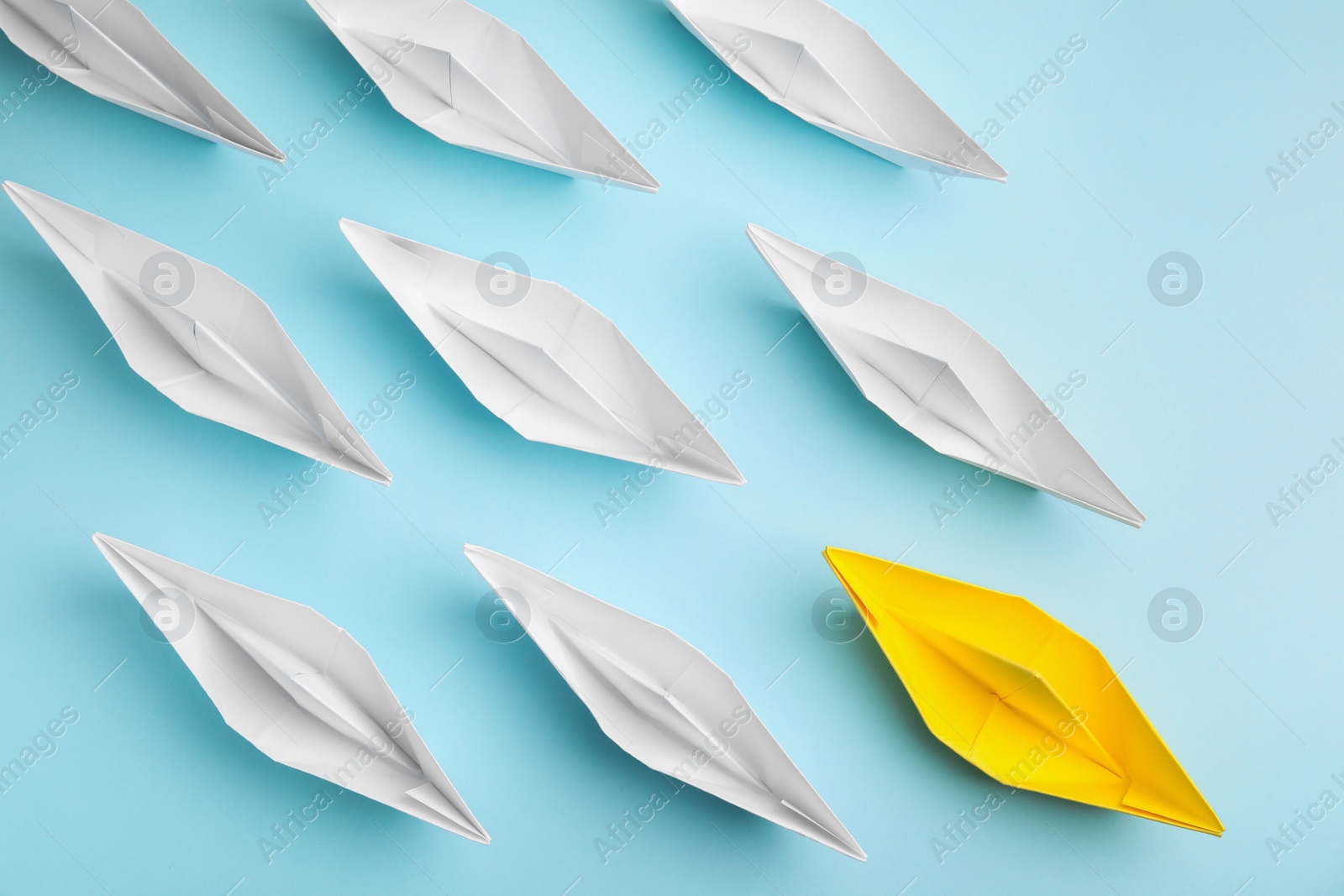 Photo of Group of paper boats following yellow one on light blue background, flat lay. Leadership concept