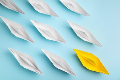 Group of paper boats following yellow one on light blue background, flat lay. Leadership concept