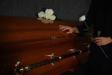 Young woman with white rose near casket in funeral home, closeup