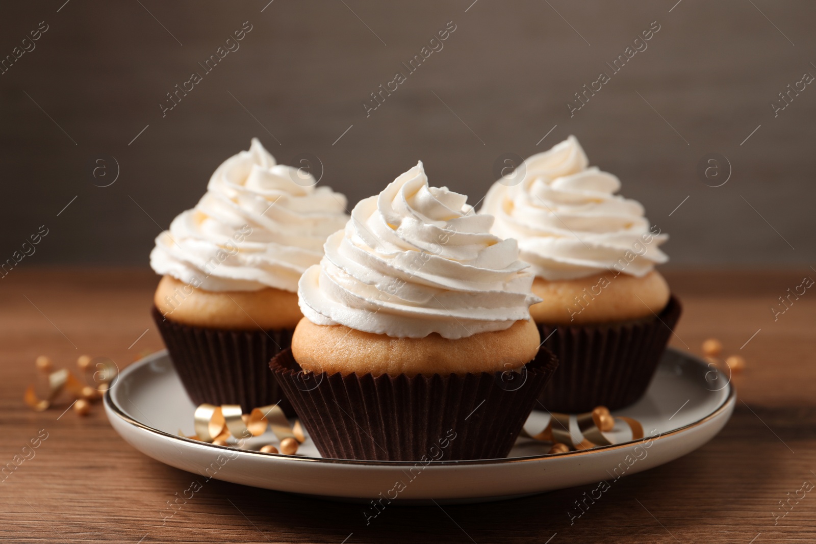 Photo of Delicious cupcakes decorated with cream on wooden table