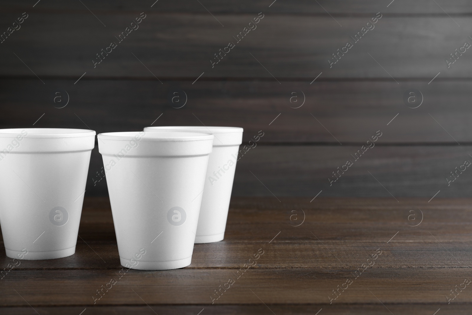 Photo of White styrofoam cups on wooden table, space for text