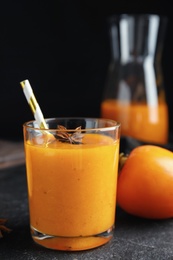 Photo of Tasty persimmon smoothie with anise and straw on black table