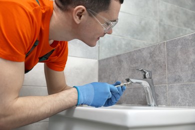 Photo of Plumber repairing faucet with spanner in bathroom