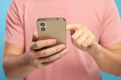 Man sending message via smartphone on light blue background, closeup