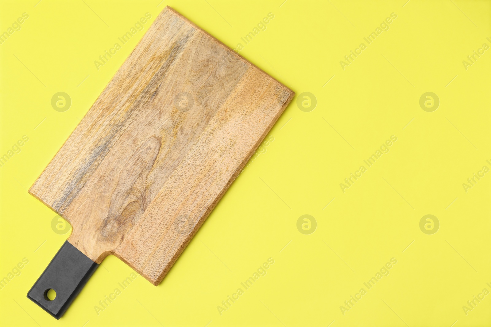 Photo of One wooden cutting board on yellow background, top view with space for text. Cooking utensil