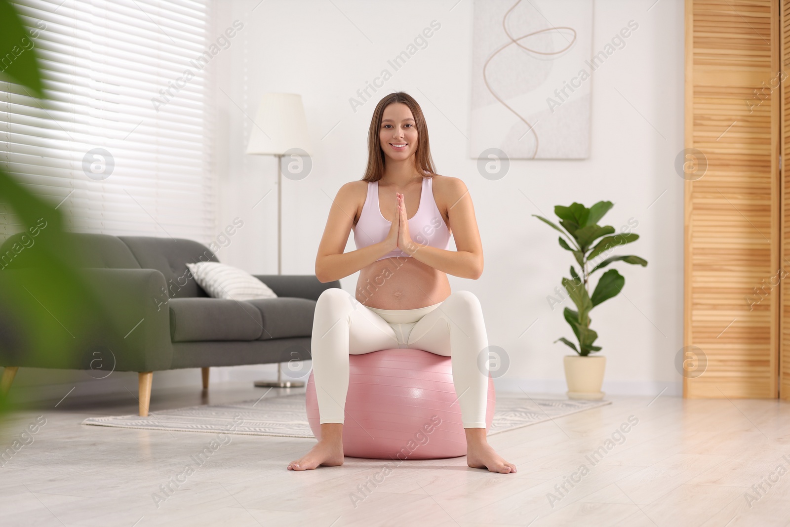 Photo of Pregnant woman meditating on fitness ball in room. Home yoga