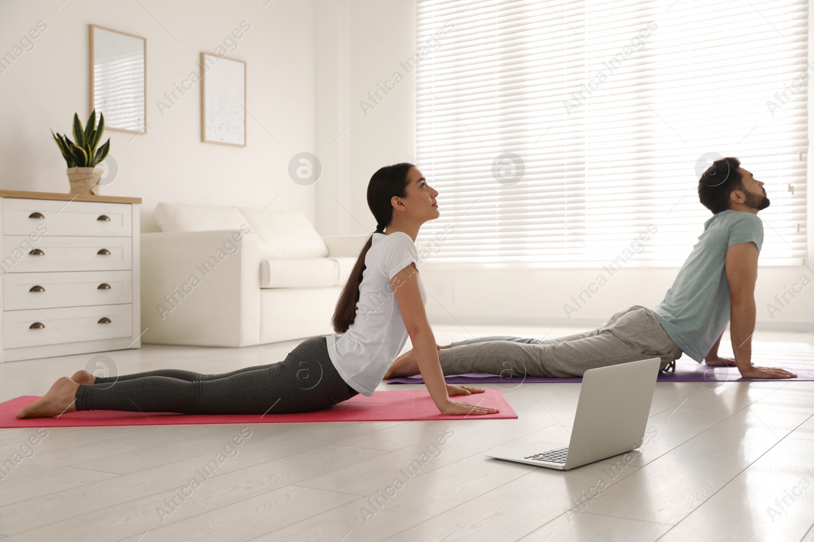 Photo of Couple practicing yoga while watching online class at home during coronavirus pandemic. Social distancing