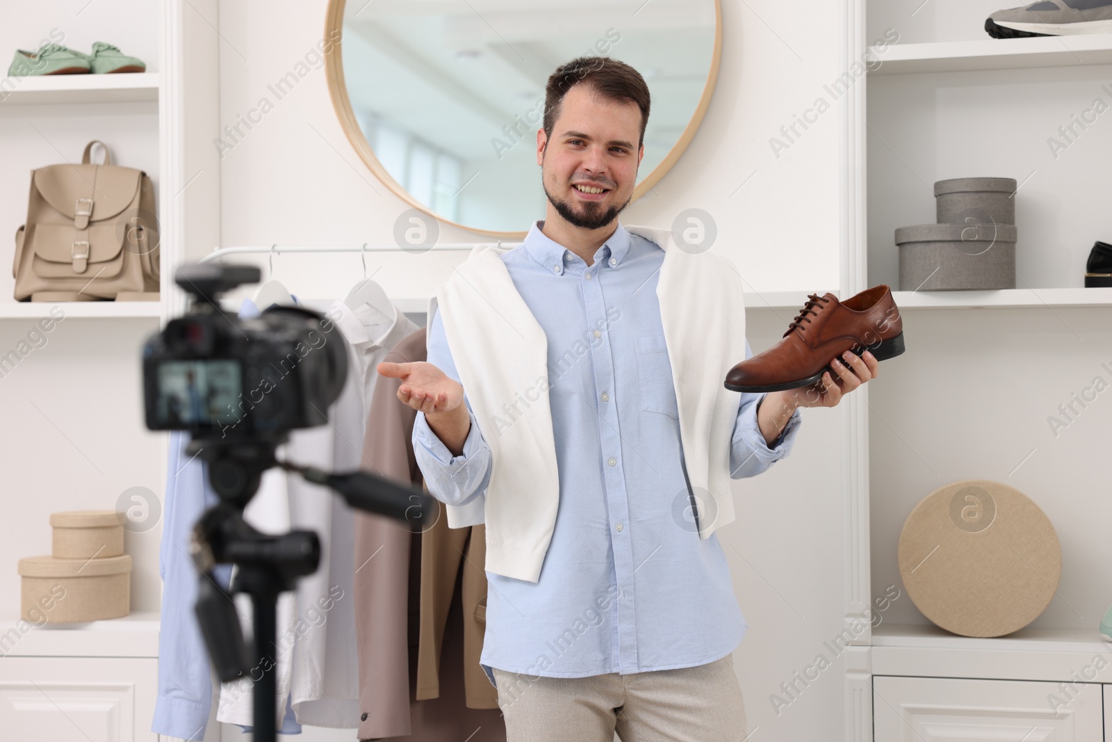 Photo of Smiling fashion blogger showing shoe while recording video at home