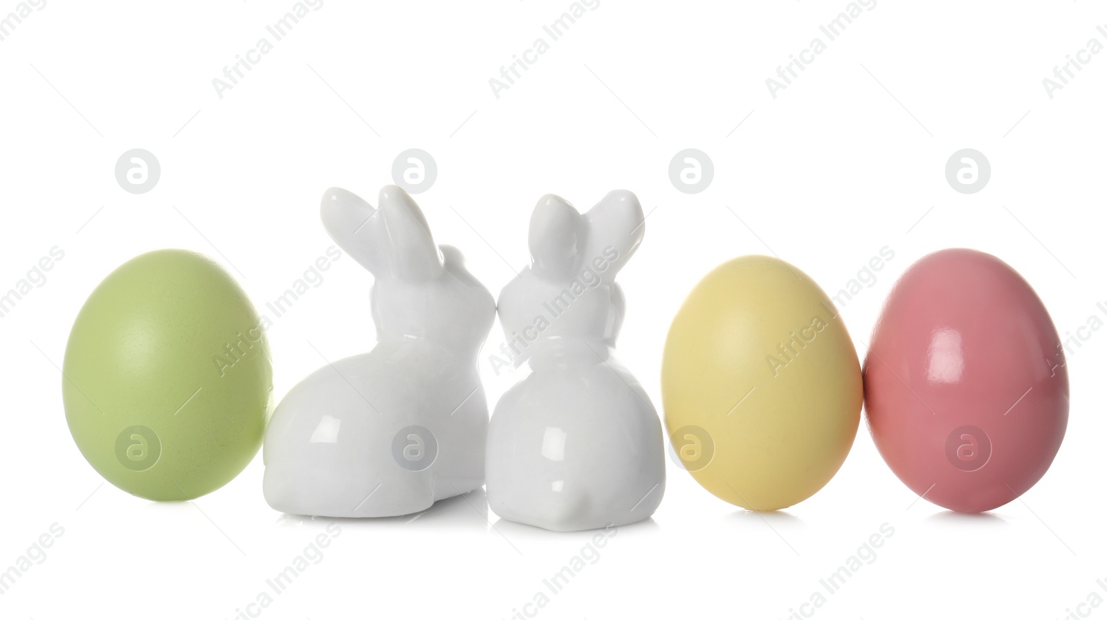 Photo of Cute ceramic Easter bunnies and dyed eggs on white background