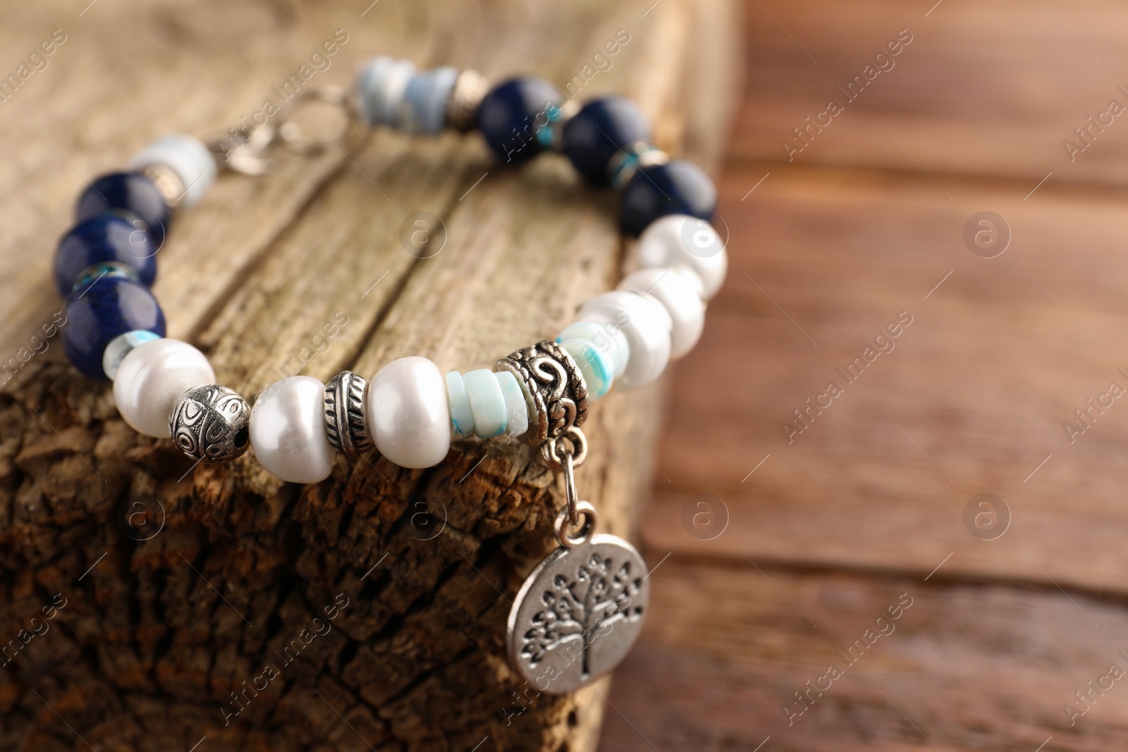 Photo of Beautiful bracelet with gemstones and decorative piece of wood on table, closeup. Space for text