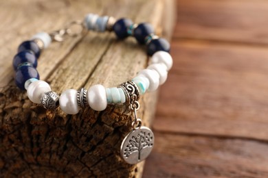 Beautiful bracelet with gemstones and decorative piece of wood on table, closeup. Space for text