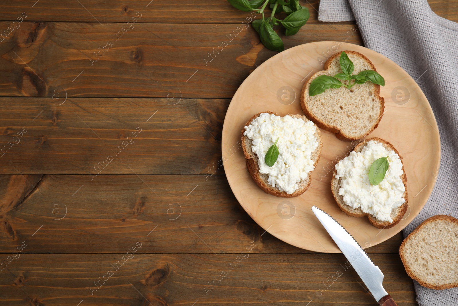 Photo of Bread with cottage cheese and basil on wooden table, flat lay. Space for text