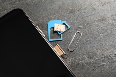 Photo of Sim card, mobile phone and ejector tool on grey table, closeup