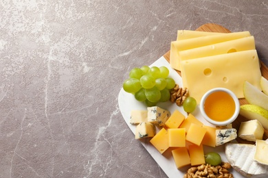 Photo of Board with different kinds of delicious cheese and snacks on marble background, top view. Space for text