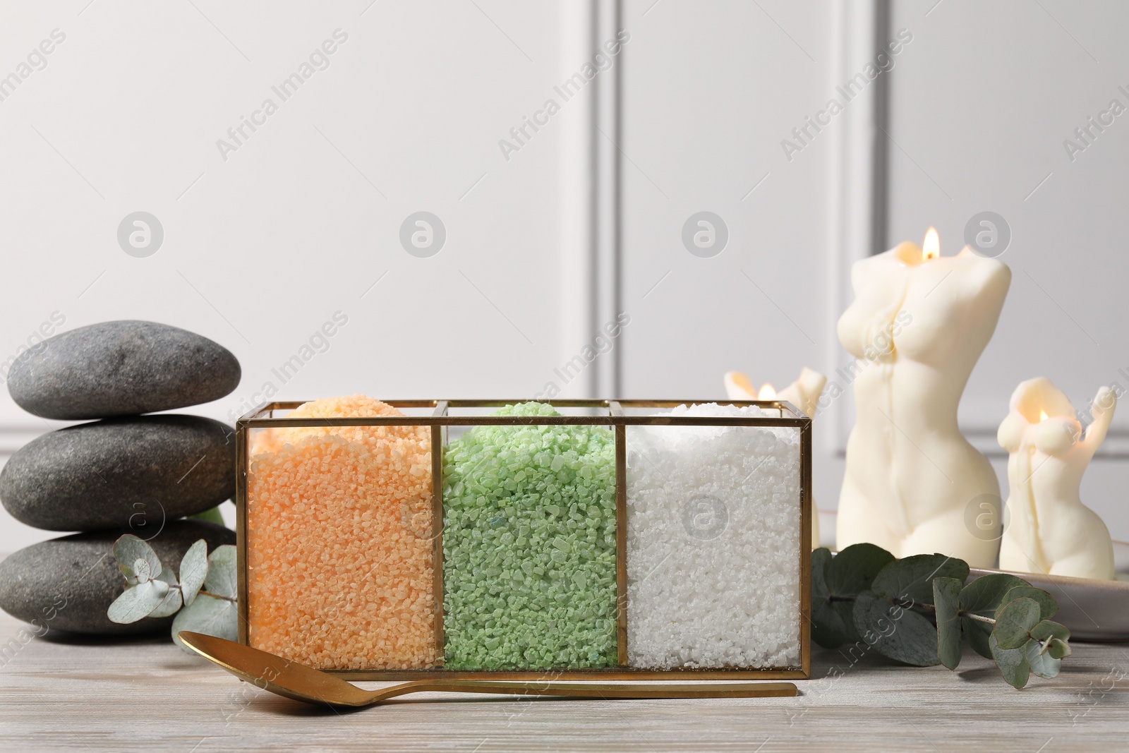 Photo of Different types of sea salt, spoon, spa stones, candles and eucalyptus branches on wooden table