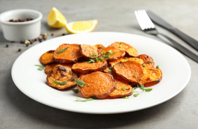 Photo of Plate with baked sweet potato slices on grey table, closeup