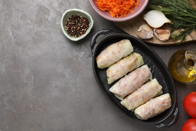 Photo of Uncooked stuffed cabbage rolls and ingredients on grey table, flat lay. Space for text