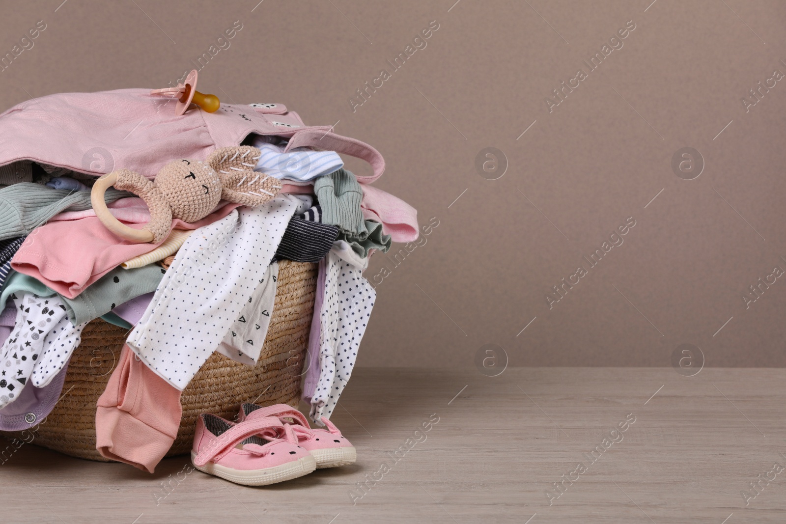 Photo of Laundry basket with baby clothes and shoes on wooden table, space for text
