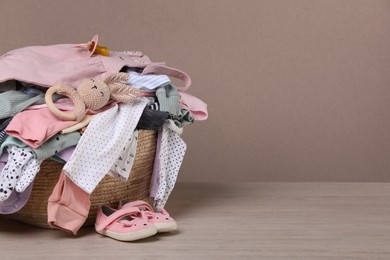 Laundry basket with baby clothes and shoes on wooden table, space for text