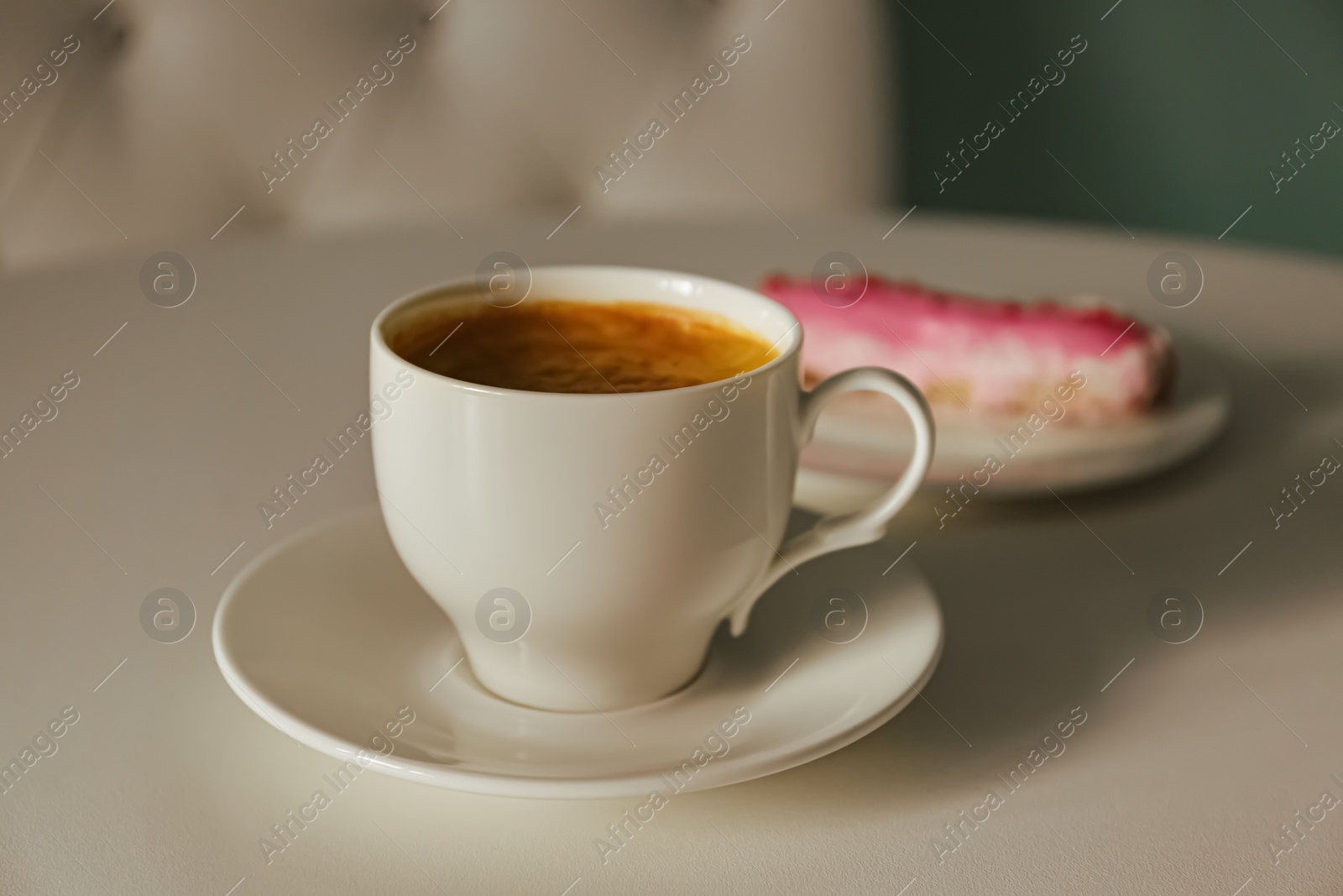 Photo of Cup of delicious aromatic coffee and eclair on white table indoors, closeup