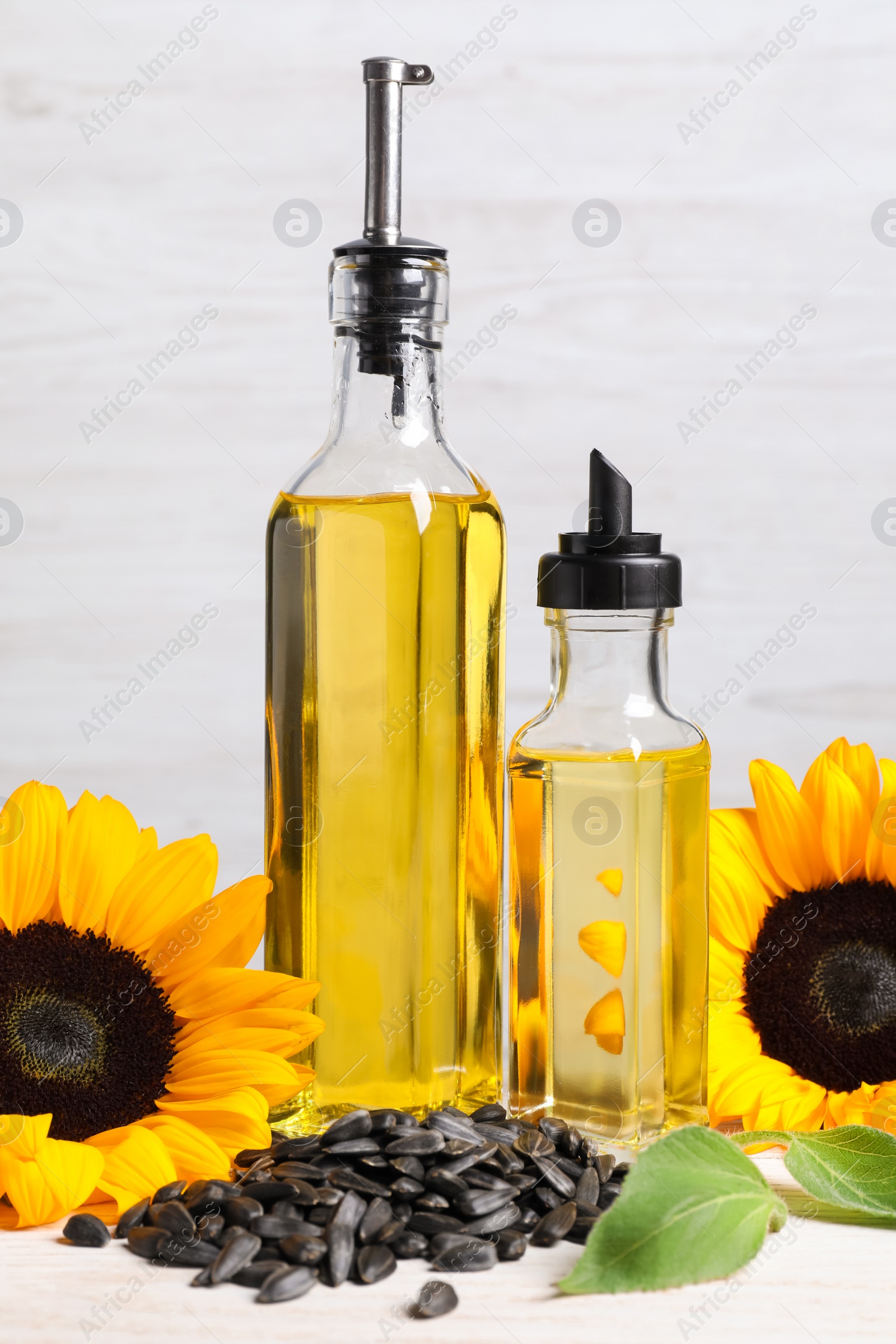Photo of Bottles of sunflower cooking oil, seeds and yellow flowers on white wooden table