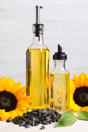 Photo of Bottles of sunflower cooking oil, seeds and yellow flowers on white wooden table