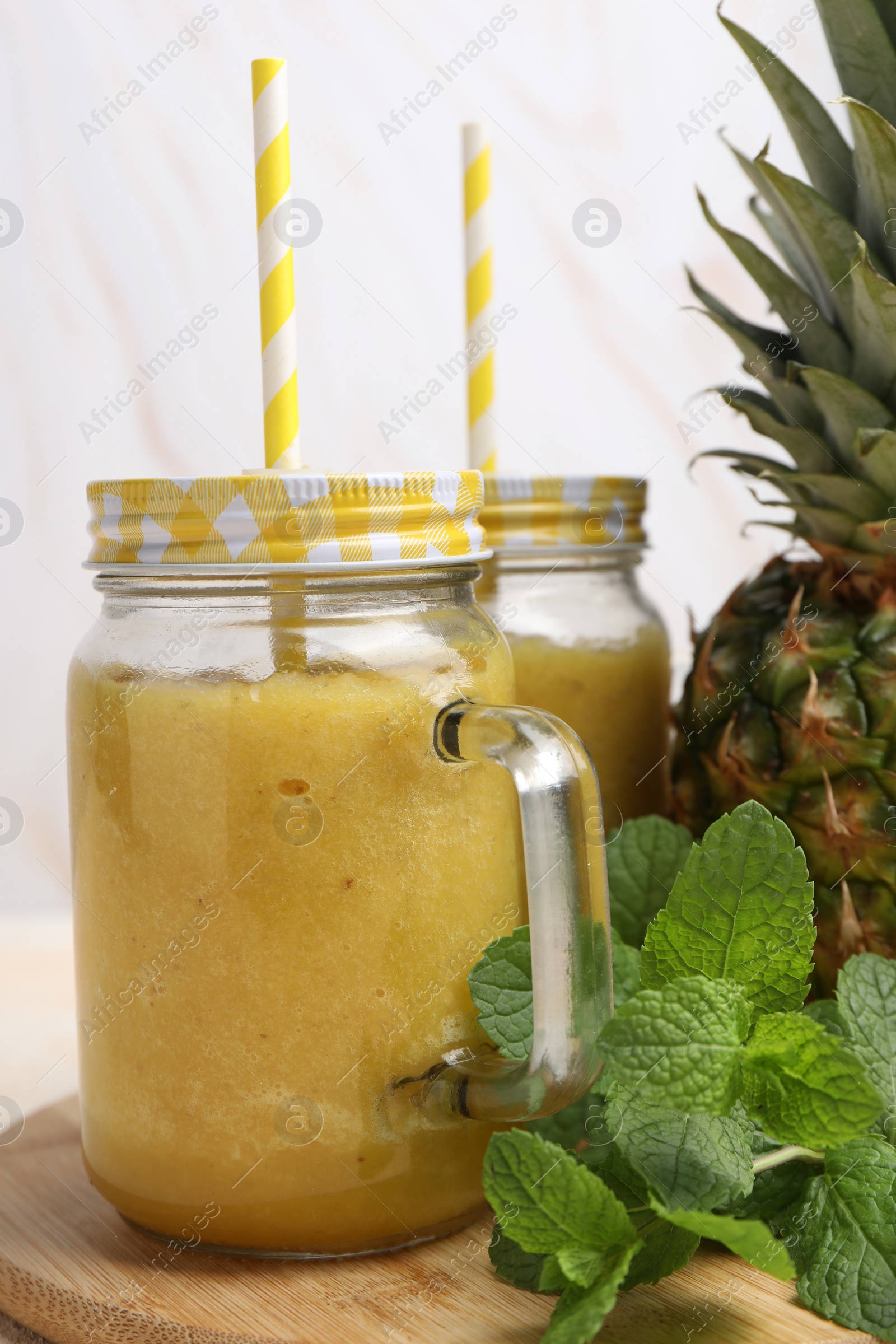 Photo of Tasty pineapple smoothie in mason jars, mint and fruit on wooden board, closeup