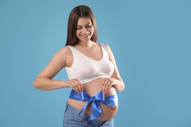 Photo of Young pregnant woman with bow on her belly against light blue background. Time to give birth