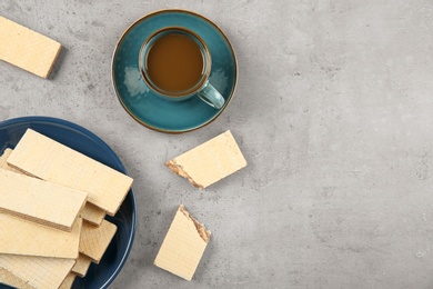 Photo of Plate of delicious wafers with cup of coffee on grey stone background, top view. Space for text