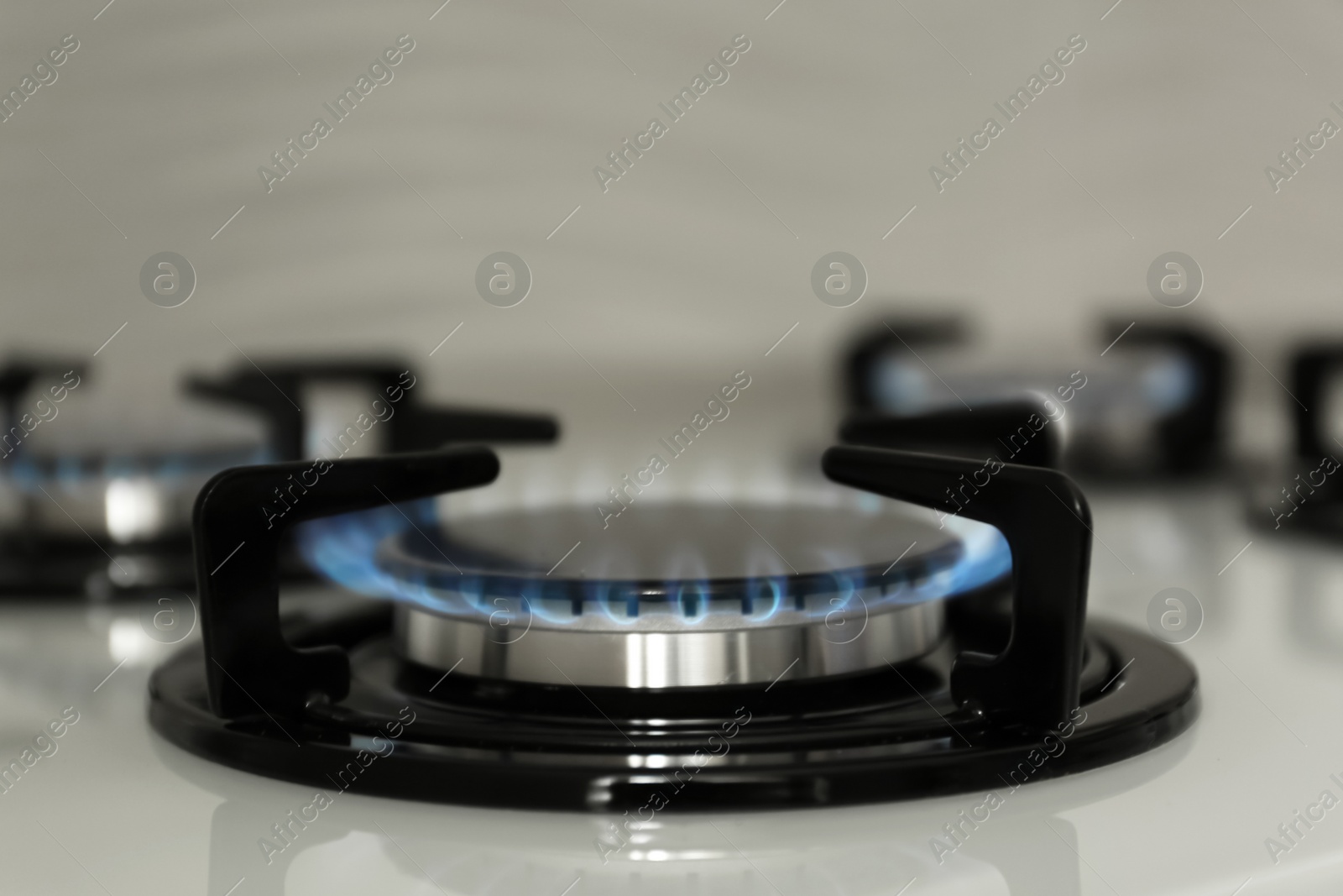 Photo of Gas burner with blue flame on modern stove, closeup. Space for text