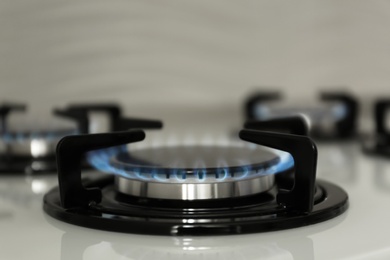 Gas burner with blue flame on modern stove, closeup. Space for text