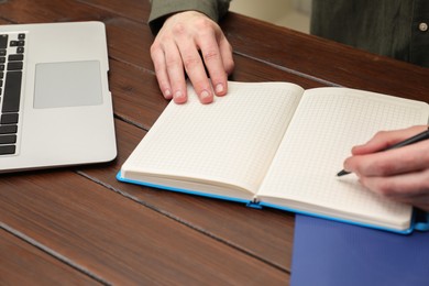 Man taking notes at wooden table, closeup