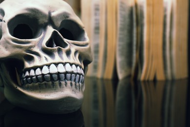 Photo of Human skull and old book on mirror table, closeup. Space for text