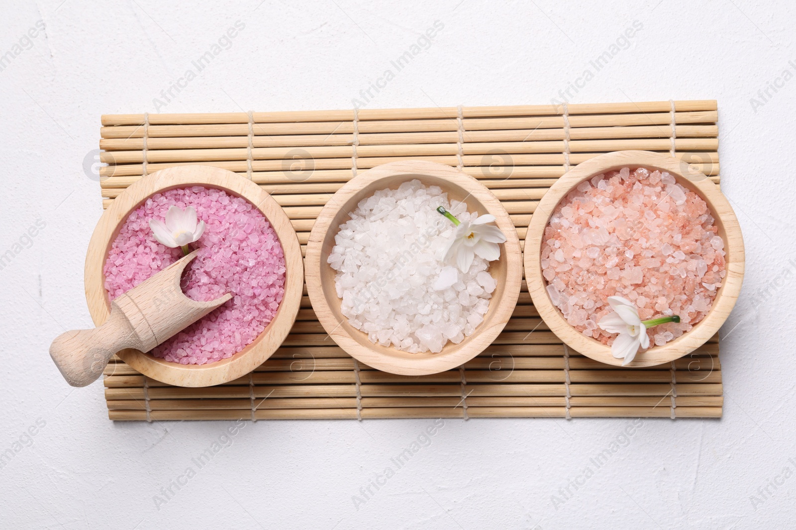 Photo of Different types of sea salt and flowers on light table, flat lay. Spa products