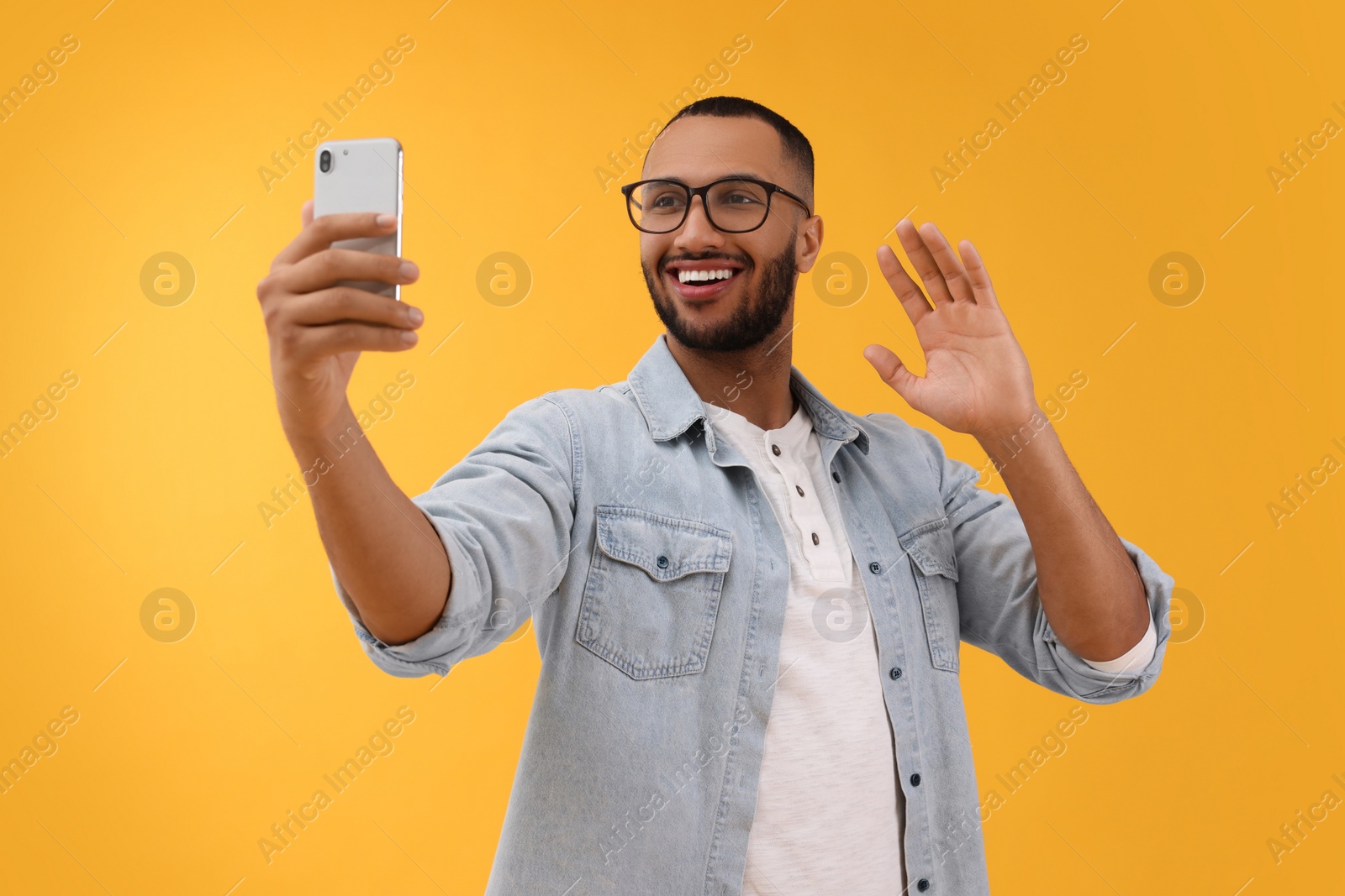 Photo of Smiling young man taking selfie with smartphone on yellow background