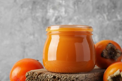 Photo of Delicious persimmon jam and fresh fruits on wooden table, closeup