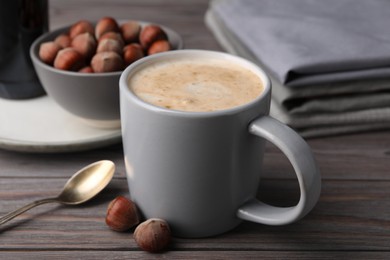 Mug of delicious coffee with hazelnut syrup on wooden table, closeup