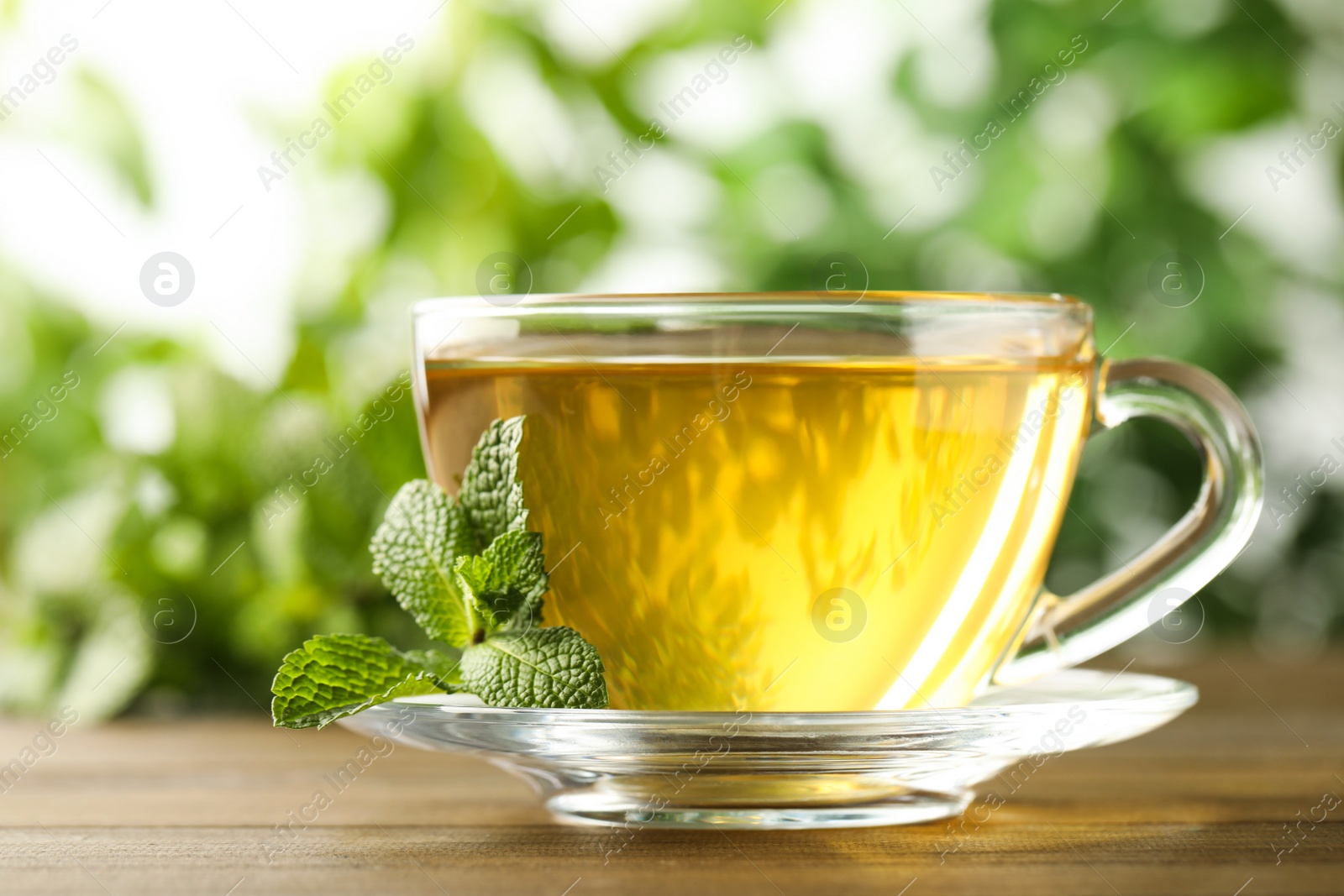 Photo of Glass cup of aromatic green tea with fresh mint on wooden table against blurred background, closeup