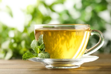Glass cup of aromatic green tea with fresh mint on wooden table against blurred background, closeup