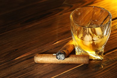 Photo of Glass of whiskey with ice cubes and cigars on wooden table. Space for text