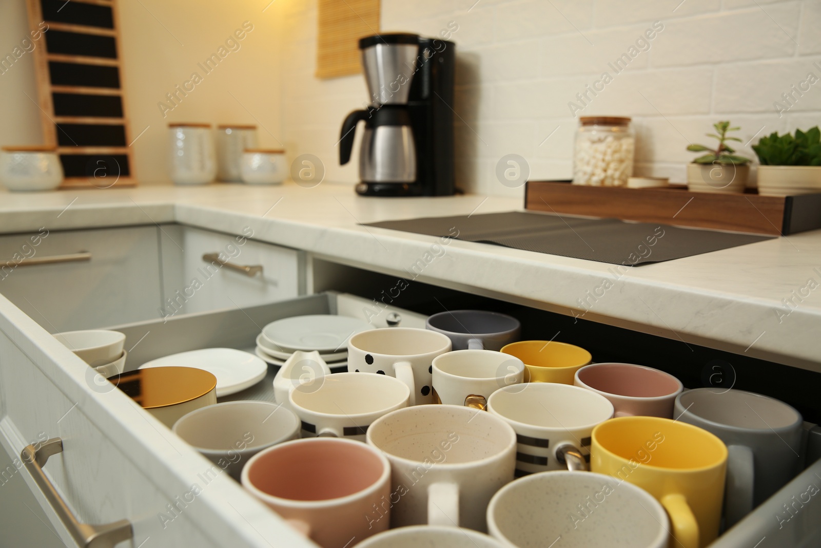 Photo of Open drawer with cups and coffeemaker on countertop in kitchen