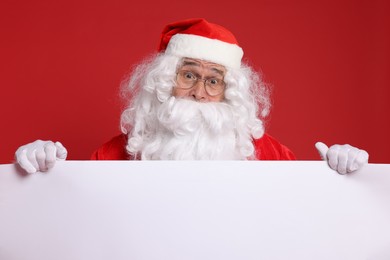 Photo of Surprised Santa Claus holding blank poster on red background. Space for text