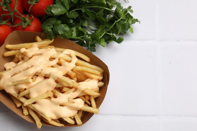 Photo of Delicious French fries with cheese sauce, tomatoes and parsley on white tiled table, closeup. Space for text