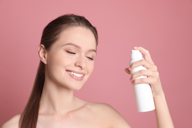 Young woman with bottle of thermal water on color background. Cosmetic product