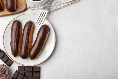 Delicious eclairs and chocolate on grey table, flat lay. Space for text