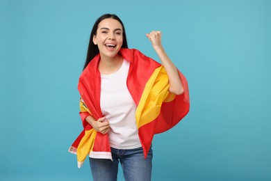 Happy young woman with flag of Spain on light blue background
