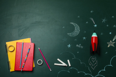 Photo of Bright toy rocket, school supplies and drawings on chalkboard, flat lay. Space for text