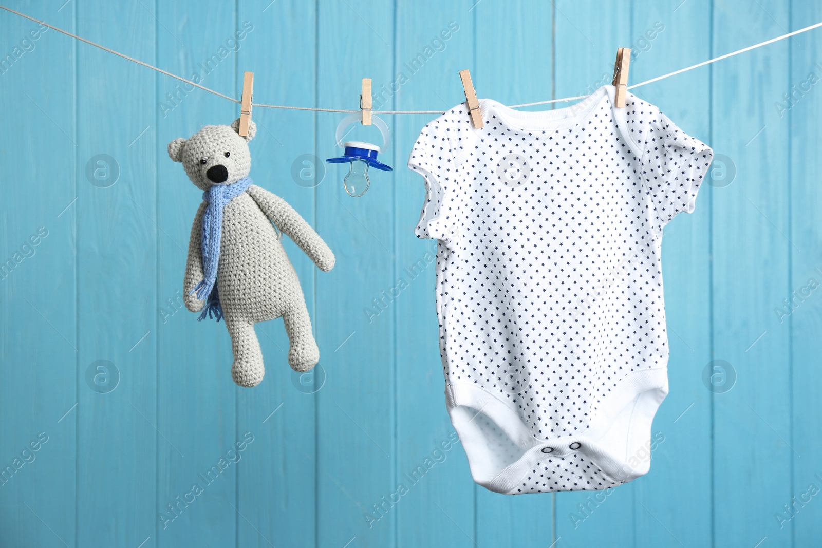 Photo of Baby accessories on laundry line against color wooden background