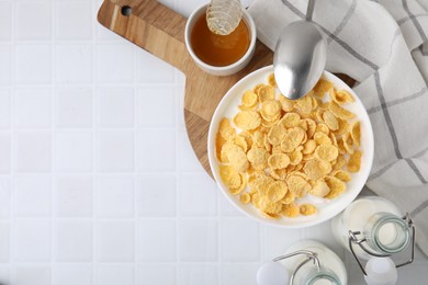 Photo of Breakfast cereal. Tasty corn flakes, milk, honey and spoon on white tiled table, top view. Space for text