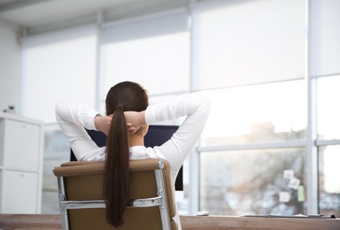 Photo of Young woman relaxing in office chair at workplace, back view